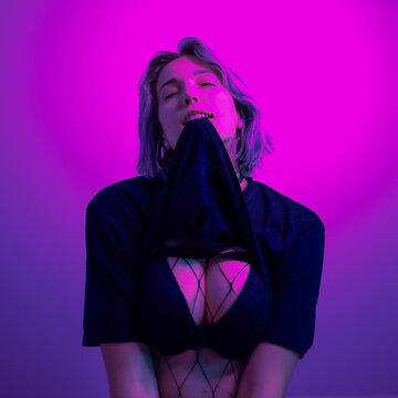 Young Woman With Short Purple Hair Lifting up Shirt to Expose Bra in Purple Light
