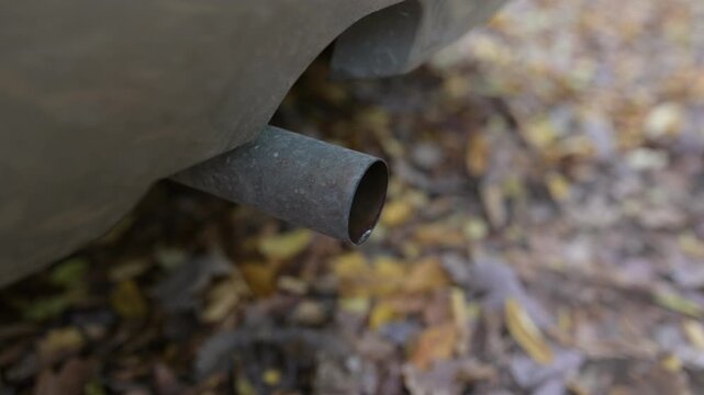 Close-up of a car exhaust pipe shaking as the engine revs, emitting bursts of condensation and sound while the vehicle accelerates. Video with sound