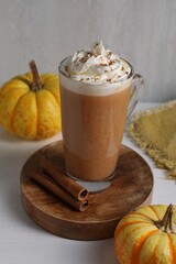 Delicious pumpkin latte with whipped cream, cinnamon sticks and fresh vegetables on white table near grey wall, closeup