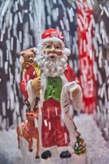 Inside a Christmas snow globe, a joyful Santa Claus figure holds a sack and stands beside a reindeer, surrounded by falling snowflakes, creating a festive holiday atmosphere