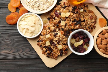 Tasty granola bars with dried fruits and nuts on black wooden table, flat lay