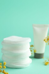 Stack of clean cotton pads, cream and flowers on turquoise background. Space for text