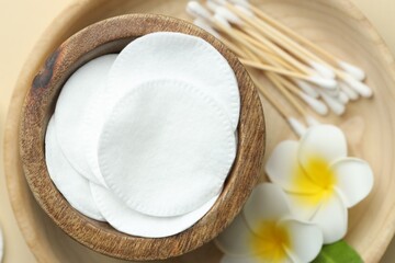 Clean cotton pads, swabs and flowers on beige background, flat lay
