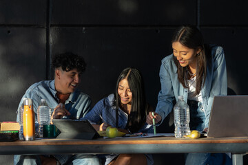 Smiling diverse group of university students collaborating outdoors around a table with laptops, books and drinks, sharing ideas and building teamwork in a bright campus setting