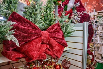 Trendy giant red bow adorns a Christmas tree display in a festive toy store, surrounded by colorful ornaments and holiday decorations, creating a joyful seasonal atmosphere