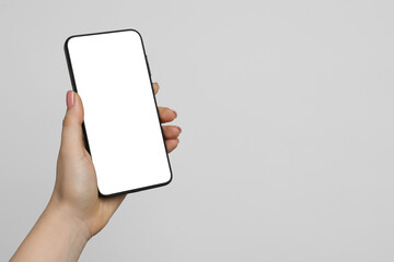 Woman holding smartphone with blank screen on light grey background, closeup. Mockup for design