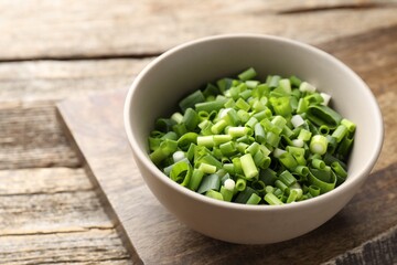 Bowl with cut green onions on wooden table, closeup. Space for text
