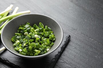 Whole and cut fresh green onions on black table, closeup. Space for text
