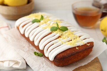 Tasty lemon cake decorated with icing, zest and mint served on white tiled table, closeup