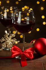 Glasses of red wine and Christmas decor on wooden table against background with blurred lights