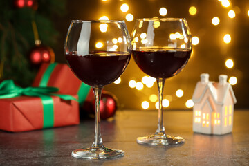 Glasses of red wine and Christmas decor on grey table against background with blurred lights