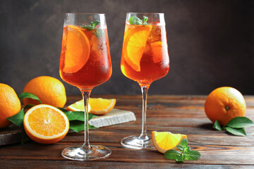 Glasses of refreshing spritzer cocktail and oranges on wooden table