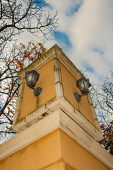 Vintage street lamps on a yellow architectural column under a bright blue sky