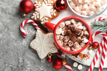 Tasty cocoa with marshmallows, candy canes, gingerbread cookies and Christmas decor on grey table,...