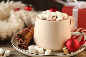 Tasty cocoa with marshmallows, candy canes, cinnamon and Christmas decor on wooden table, closeup