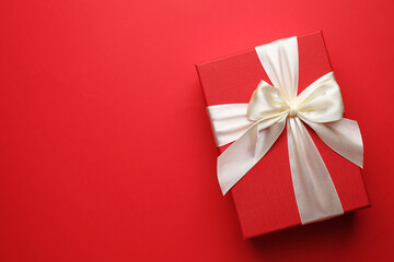 Beautiful gift with bow on red background, top view. Space for text