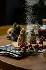 Two conical sweets are sprinkled with powdered sugar, sitting on a wooden board. Surrounding them are festive decorations, creating a warm and inviting atmosphere perfect for winter celebrations