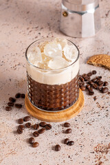 Iced creamy coffee with milk and moka pot in simple modern setup. on beige kitchen table background. Coffee break during a hot summer day, refreshing drink