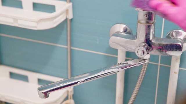 Close-up of faucet cleaning in bathroom with blue tiled wall