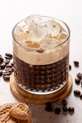 Espresso creamy iced coffee with scattered coffee beans on textured stone table, close up