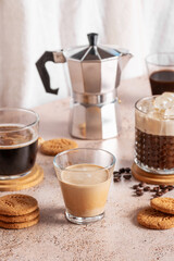 Freshly brewed espresso, iced coffee and moka pot in beige cozy kitchen setup. Different types of coffee drinks with cookies on a beige table