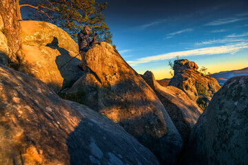 Adventure photographer shooting golden-hour mountain landscape from dramatic rocky cliffs