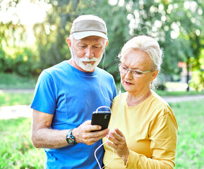 Happy active senior couple having fun using smartphone and wearing sportswear, checking music or an exercise app, after having an exercise sport activity outdoors