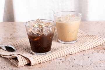 Two coffee drinks, iced latte and black espresso on beige stone textured background