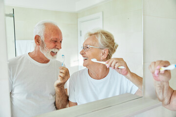 Portrait of an elderly senior couple cleaning brushing their teeth in front of mirror in bathroom. Dental hygiene, vitality, love and beauty concepts