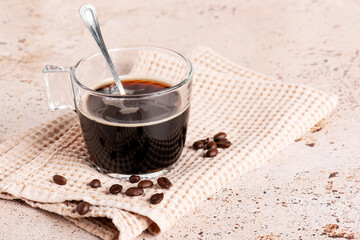 black soluble coffee in a clear glass cup with coffee beans on textured napkin on beige stone kitchen table, Coffee break, refreshing energy drink