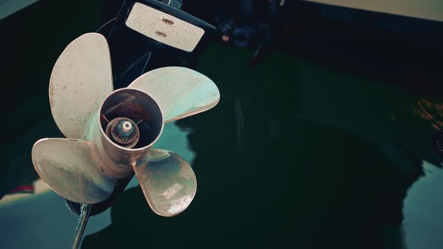 Close up view of a marine metal propeller partially submerged, showing rust, patina, and subtle reflections of blue green water