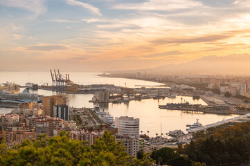 View of port with buildings, embankment, cranes, boats and yachts in Malaga city at golden hour, Andalusia, Spain. Cityscape at sunset.
