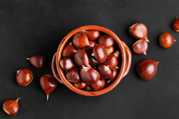 Raw chestnuts in a rustic clay bowl on black background, close up
