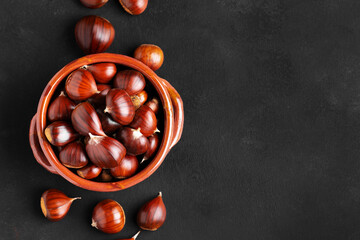 Raw chestnuts in a rustic clay bowl on black background, web banner, copy space