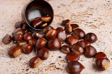 Autumn raw chestnuts in rustic wooden bowl on beige stone kitchen table background, close up