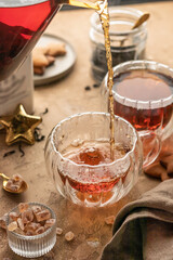 Pouring black tea into transparent glass cup from teapot on brown textured table background. Frozen spalshes of tea in cup