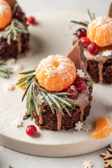 Chocolate brownie cakes with festive decor with tangerines on white tray close up. Christmas or New Year food ideas sweet homemade pastry concept. Holiday cooking