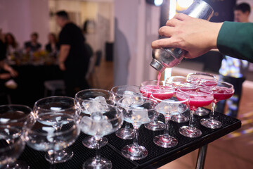 Mood setting with lively drink preparation at upscale bar, Elegant scene of bartender pouring colorful cocktail amidst festive warm lighting and guests in background