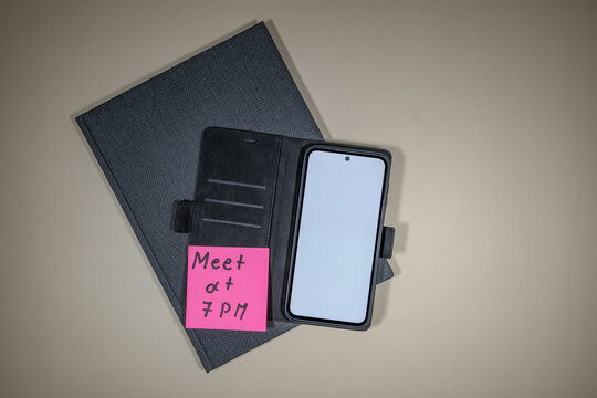 Notizbuch und Mobiltelefon mit Notizzettel "Meeting at 7 PM"