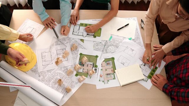 Architect and safety engineer discussion about building construction use blueprint on table with architectural document, measurement tool and wooden block scatter around at modern office. Delineation.
