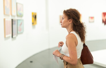 Thoughtful woman in her middle ages gazing at displayed objects in exhibition hall