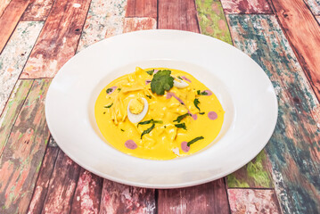 A bowl of vibrant yellow Peruvian aji amarillo cream, with a silky texture, served with chunks of white potato, hard-boiled egg, and botija olives