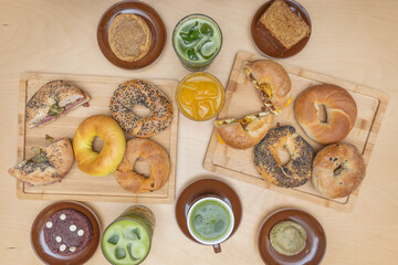 A still life with an onion bagel cut open to reveal its filling, a bottle of craft beer, and a glass of cider, on a rustic wooden surface