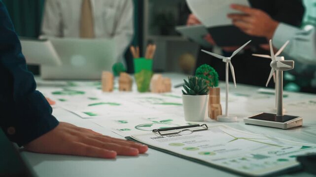 A diverse business team collaborates on a renewable energy project, surrounded by wind turbine models and green plants, highlighting their commitment to sustainability and innovation. SACTR