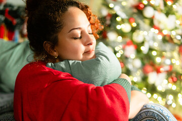 Woman finding comfort, hugging pillow near christmas tree