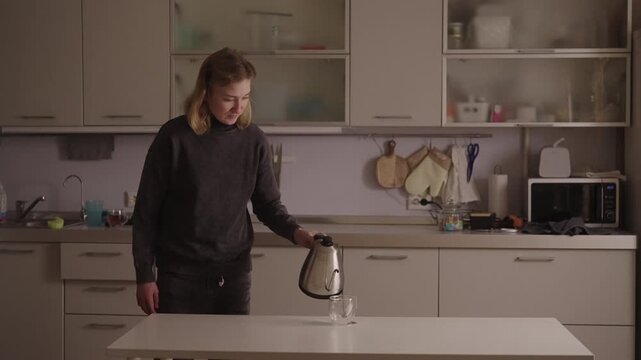 Portrait of independent woman with cerebral palsy performing common household task, pouring hot water for tea in kitchen, demonstrating perseverance and ability in everyday life, slow motion.