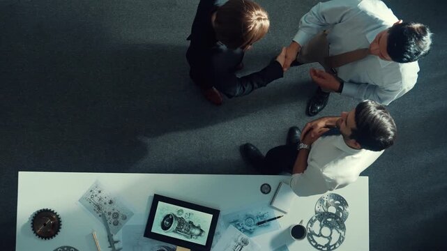 Top down view of smart engineer talking about turbine engine design while standing at meeting table with gear. Aerial view of technician discussing and shaking hand or making a contract. Alimentation.