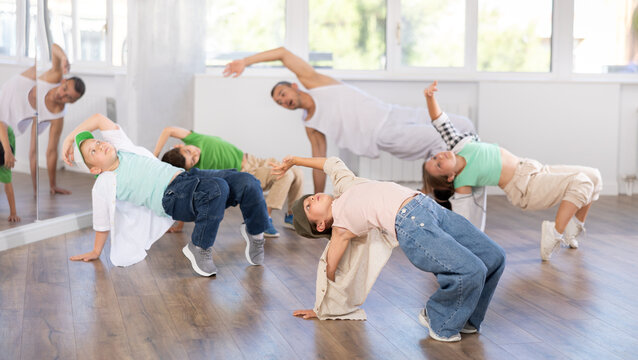 Focused preteen girl performing dynamic hip hop moves in group class for kids, led by skilled young male dance instructor in vibrant urban studio