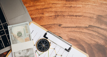 Business concept. Stack of money compass clipboard laptop financial chart wooden table business planning investment strategy office desk navigation tool