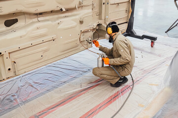 Specialist spraying anti rust sealant into the hidden chassis cavities. Protection against corrosion and internal body element sealing in a professional auto service shop